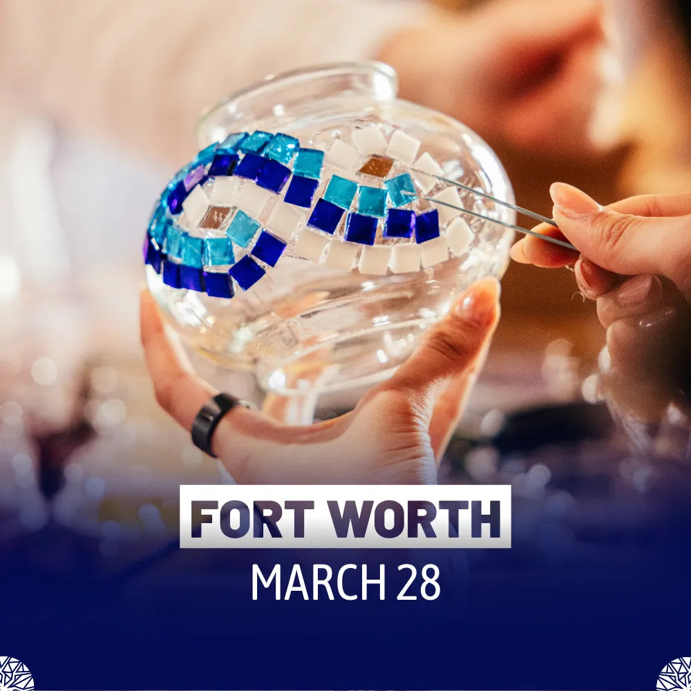 Hands placing blue and white mosaic glass tiles in wave pattern on glass sphere using tweezers at Mosaic Lamp Workshop Fort Worth Texas by Tiles Workshop