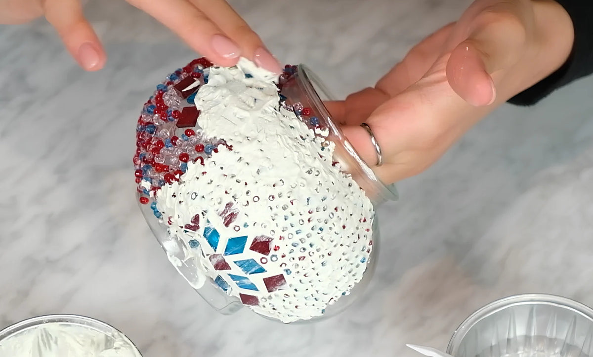 Spreading white grout over a mosaic lamp globe