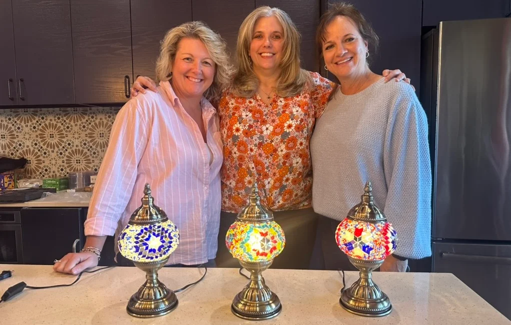 Three friends smiling behind the Turkish mosaic lamps they made